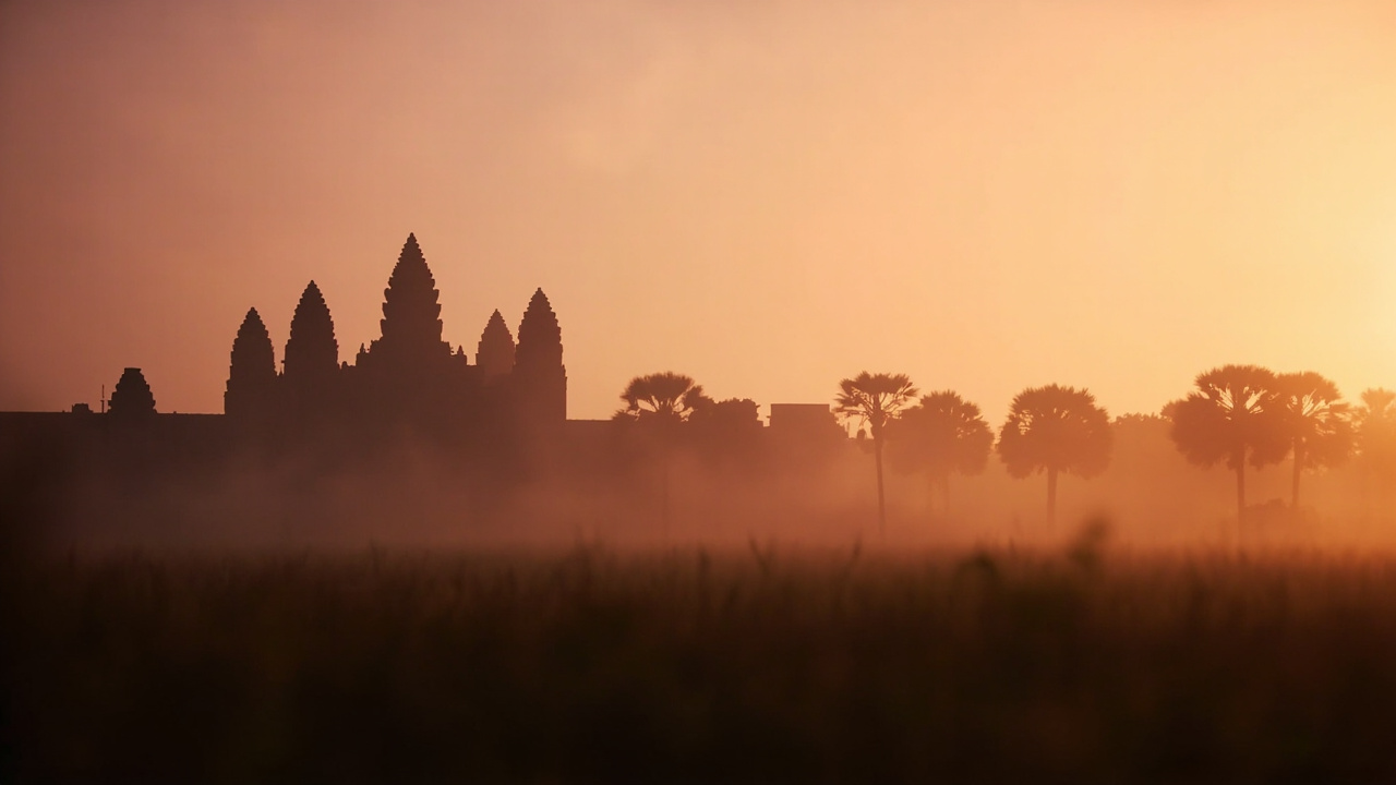 Generic Khmer-style temple silhouette at warm dawn light with soft mist in the foreground, an Angkor-like Cambodia temple alternative to the Myanmar pagoda imagery